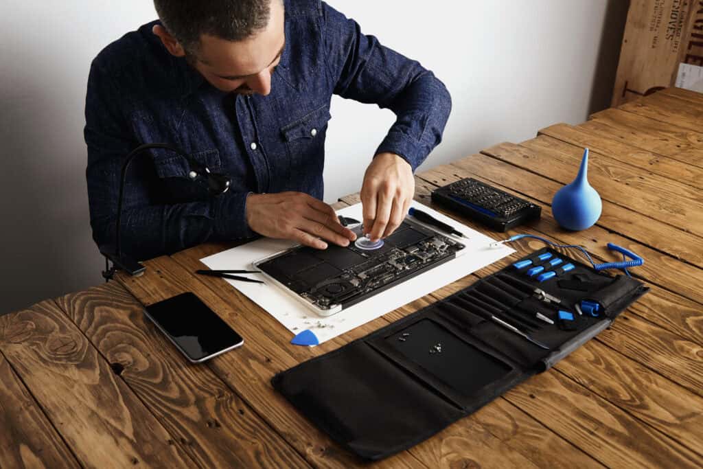 Technician repairing a laptop with tools on a wooden desk.
